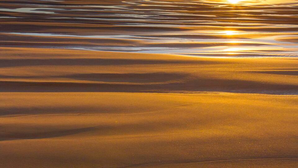 A sunset over a sandy beach with waves and a rock formation.