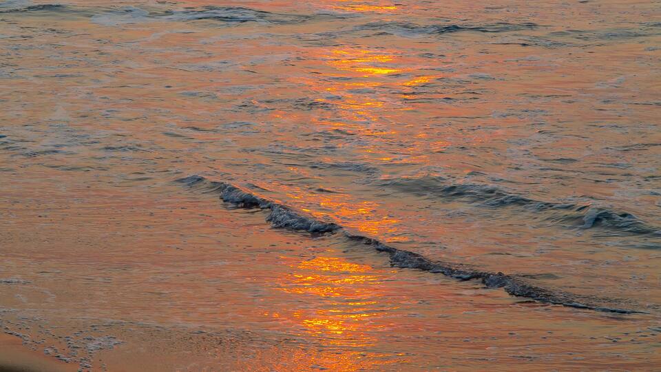 A sunset over the ocean with waves crashing onto the shore.