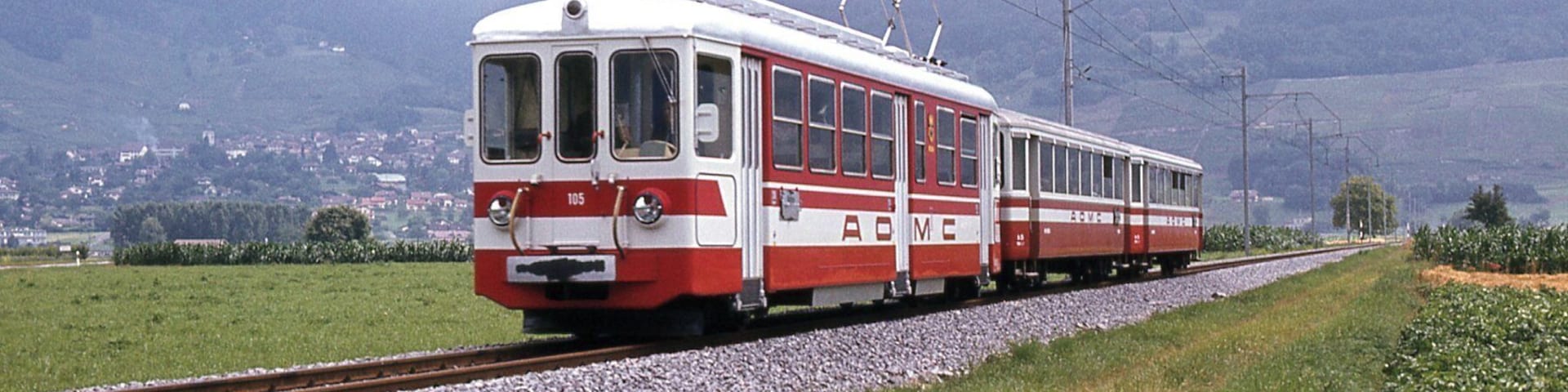 Photo: Trams aux Fils. Prise après 1985 Vers Villy Motrice du B.L.T. aux couleurs A.O.M.C. avec deux voitures A.O.M.C. La ligne Aigle Ollon Monthey Champéry a été inaugurée en 1907 pour la portion d'Aigle Ollon Monthey et en 1908 pour la portion Monthey Champéry à voie métrique et à crémaillière, sa longueur est de 23 Kilomètres. Cette compagnie est le fruit de la fusion en 1946 de deux compagnies Aigle Ollon Monthey et Monthey Champéry Morgins.
