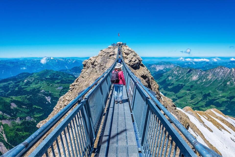 Une personne se tient sur un pont métallique, avec un paysage montagneux en arrière-plan.