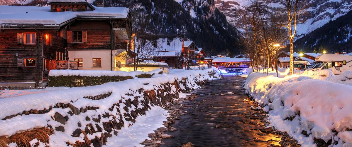 A snow-covered mountain path with wooden buildings and a lit street.