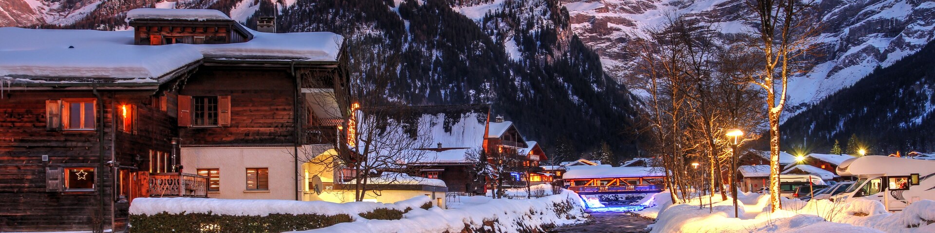 A snow-covered mountain path with wooden buildings and a lit street.