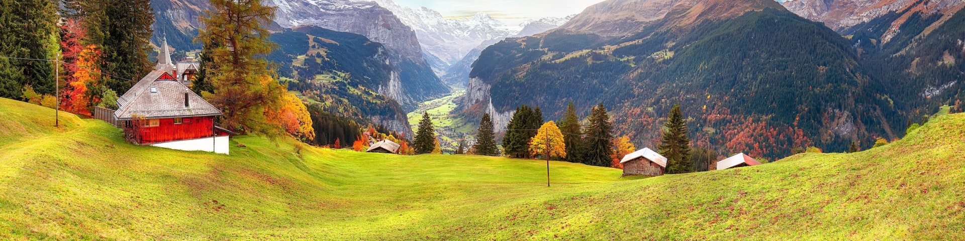 A mountainous landscape with a red barn, green fields, and autumn-colored trees.