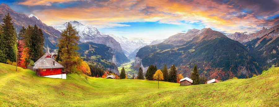 Eine Berglandschaft mit einem roten Bauernhaus, grünen Feldern und herbstlich gefärbten Bäumen.
