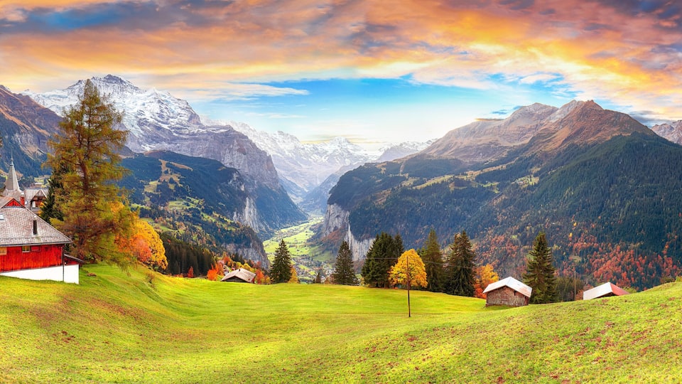 A mountainous landscape with a red barn, green fields, and autumn-colored trees.