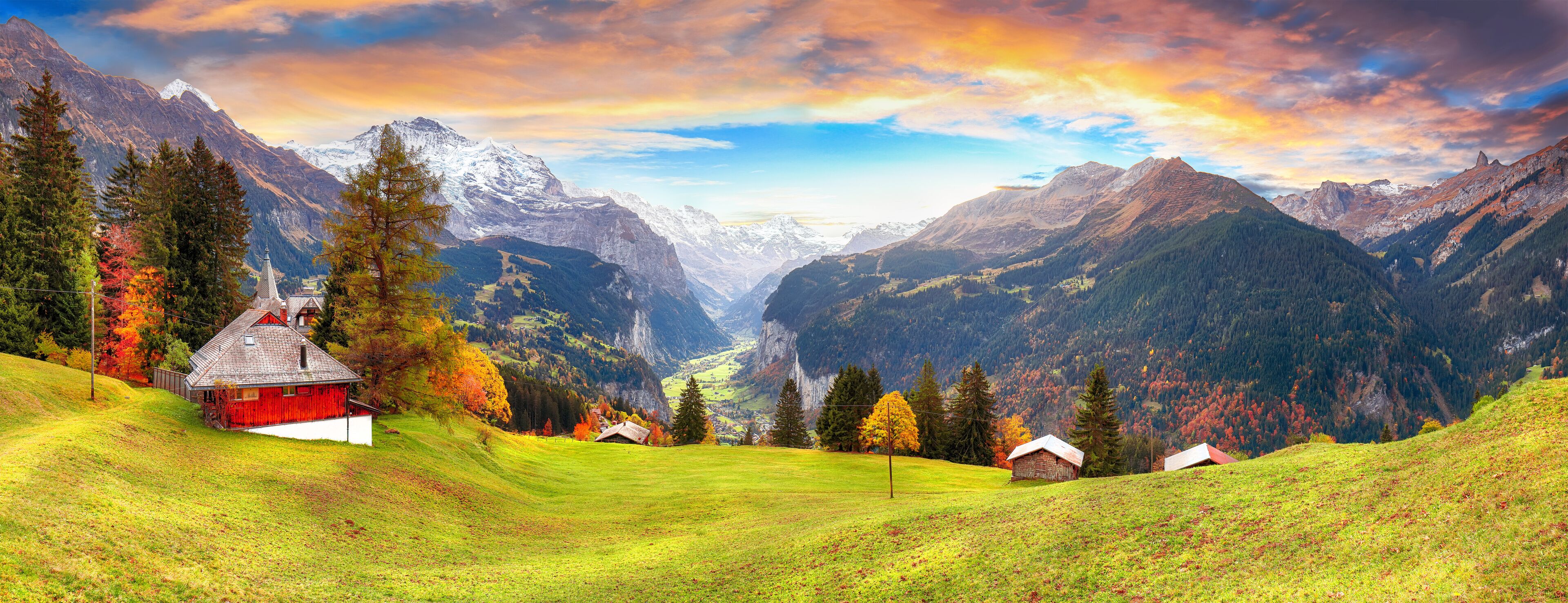 A mountainous landscape with a red barn, green fields, and autumn-colored trees.