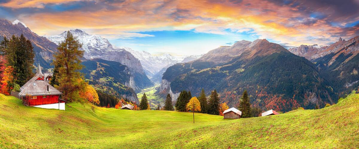 A mountainous landscape with a red barn, green fields, and autumn-colored trees.