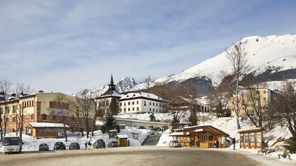 Ein verschneites Bergstädtchen mit Kirche, Bus und einer Holzhütte.