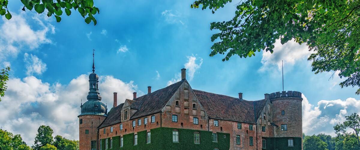 A historic building with a tower, surrounded by a moat and lush greenery.