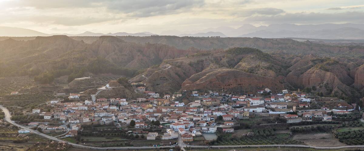A town nestled in a mountainous valley with winding roads and red-roofed buildings.