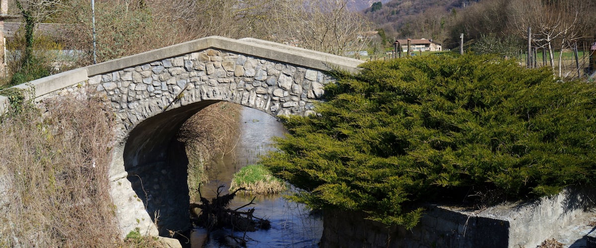 A stone bridge over a river with snow-capped mountains in the background.