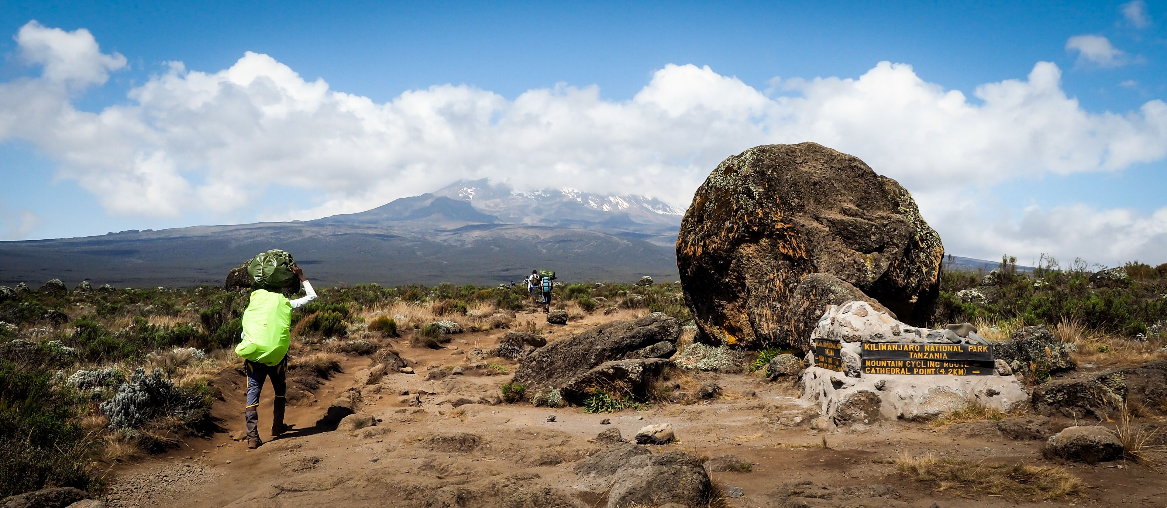 A hiking trail with a large rock and a sign for Kilimanjaro National Park.