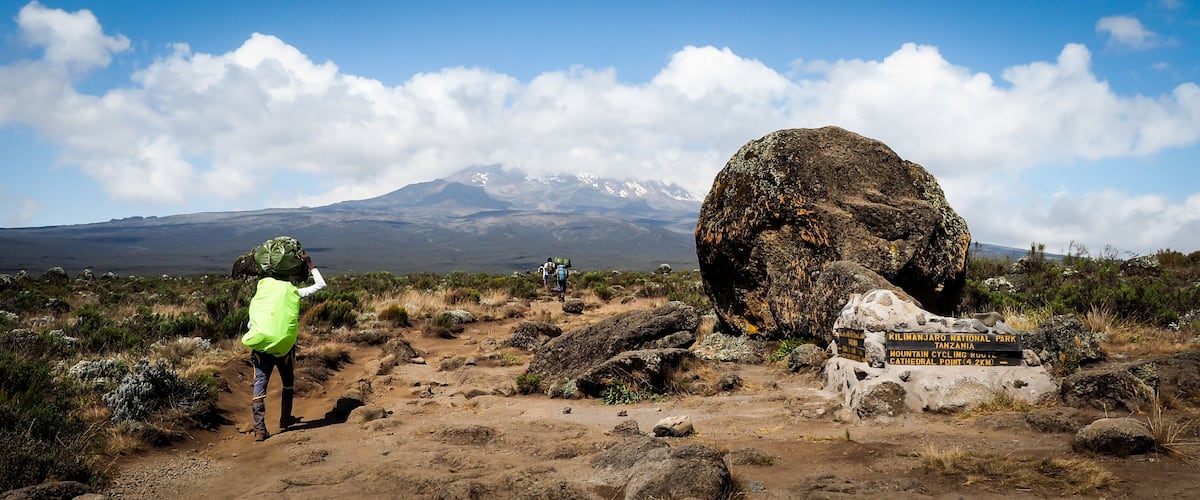 A hiking trail with a large rock and a sign for Kilimanjaro National Park.