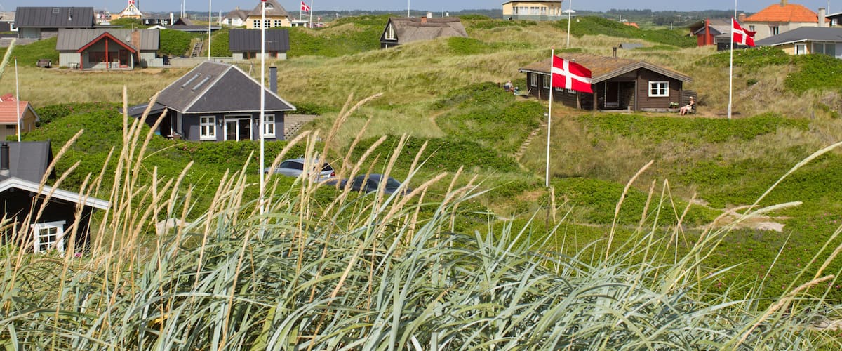 A coastal village with houses on grassy dunes, a windmill, and a flag.
