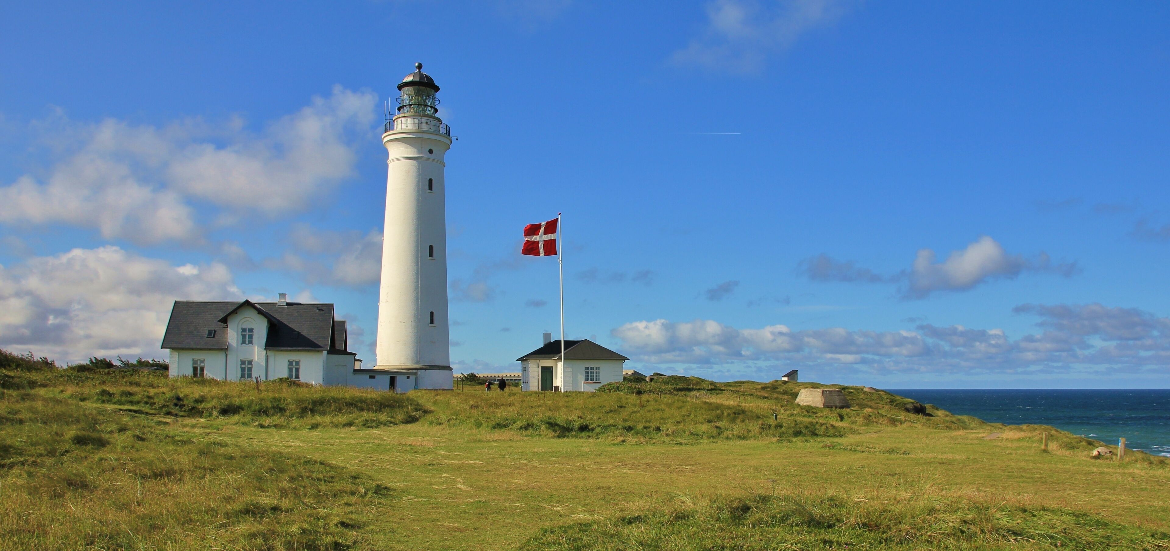 A lighthouse, a grassy field, and a building with a flag.
