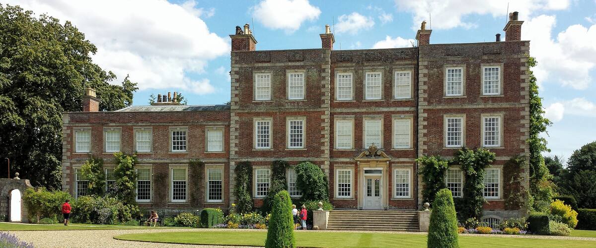 A large, historic brick building with multiple windows and a well-maintained garden in front.