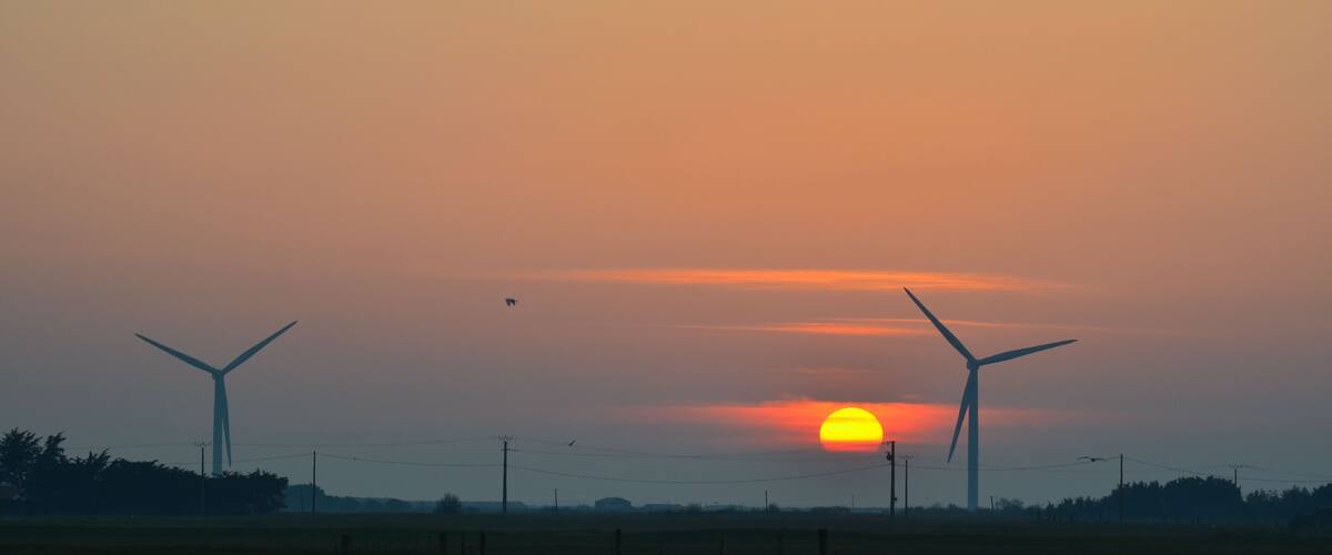 A sunset over a wind farm with two large wind turbines silhouetted against the sky.