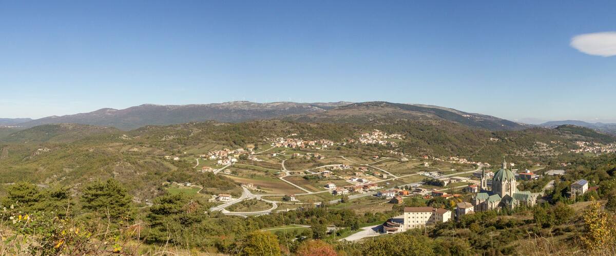 A mountainous landscape with a winding road, a church, and scattered buildings.