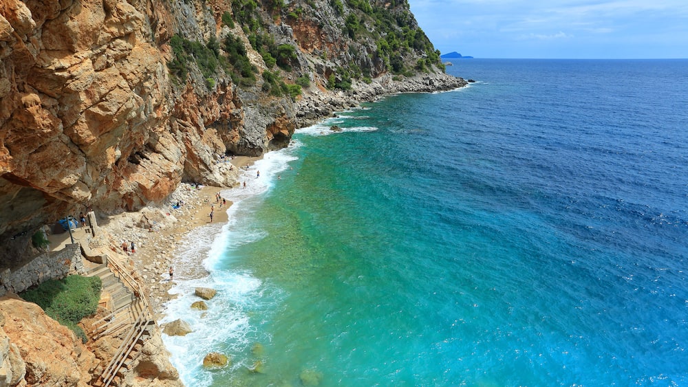 Un paysage côtier caractérisé par des falaises rocheuses, des eaux turquoise et limpides, et une île visible au loin.
