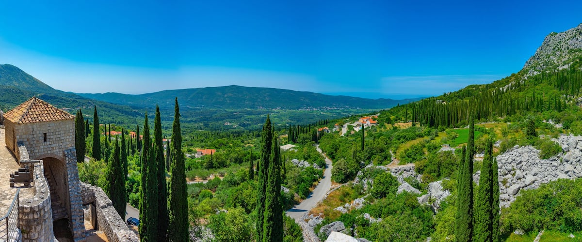 A stone tower, a winding road, and a village nestled in a valley surrounded by mountains.