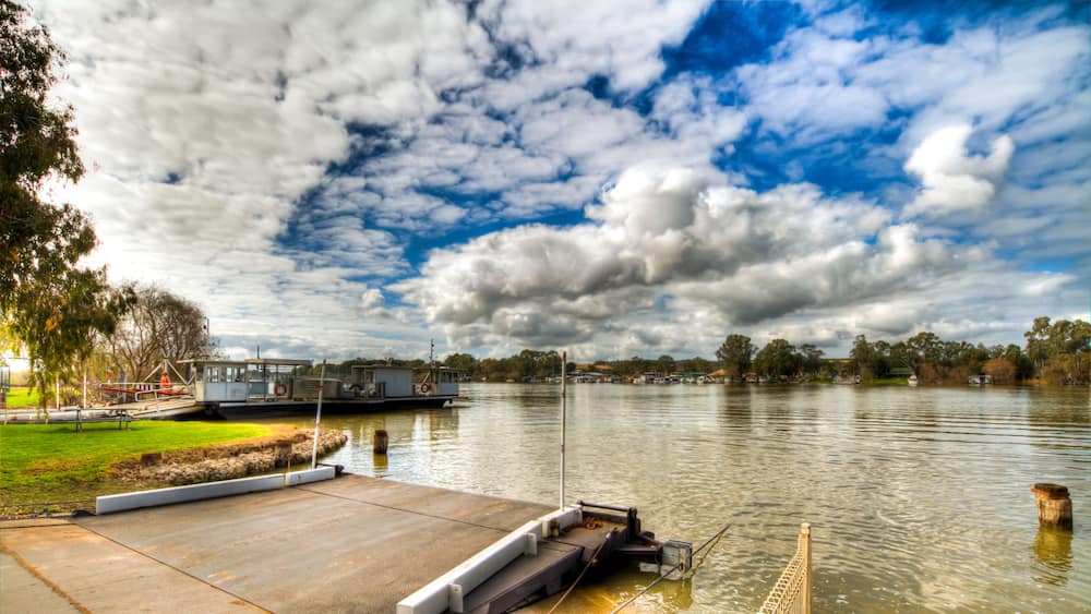 Ein Flusskai mit einer Betonplattform, ruhigem Wasser und einem teilweise bewölkten Himmel.