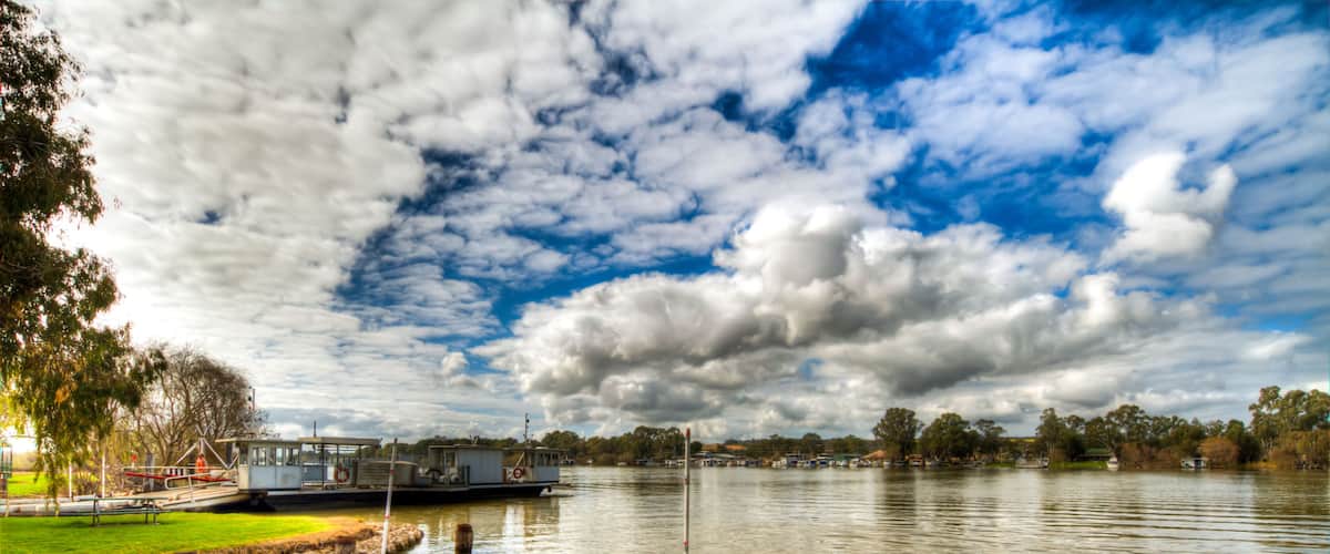 A riverside dock with a concrete platform, calm water, and a partly cloudy sky.