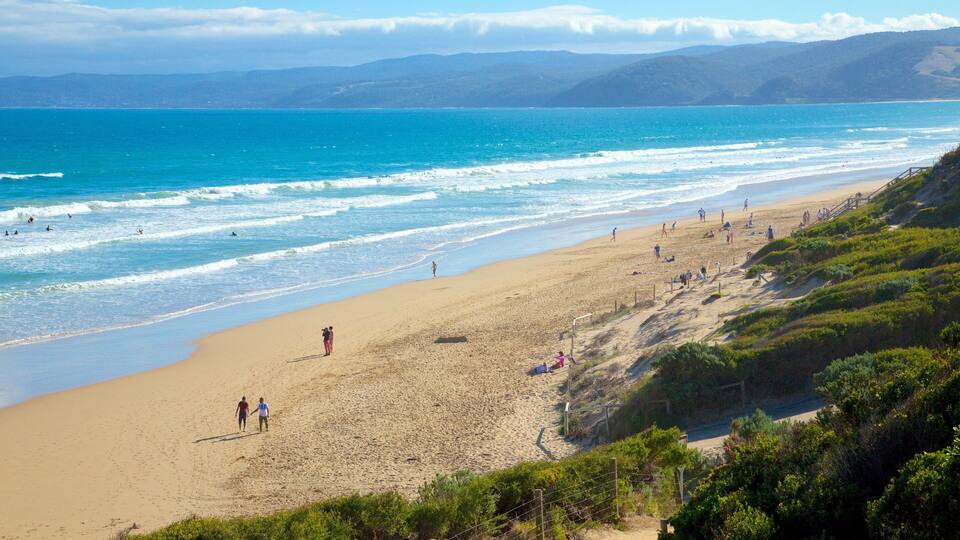 A beach with people walking and swimming, surrounded by hills and a clear sky.