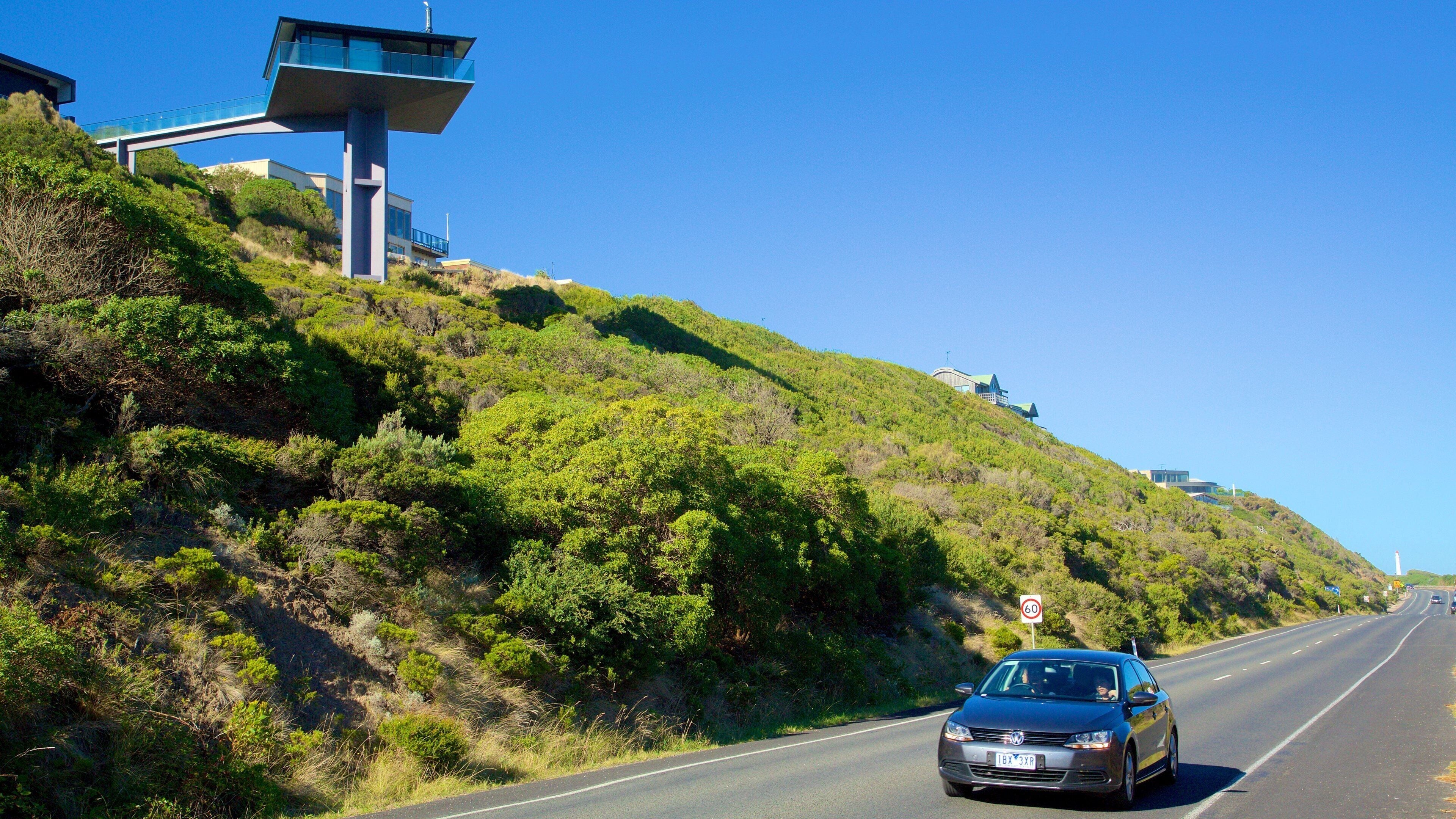 A car driving on a road with a speed limit sign of 60, surrounded by lush greenery and hills.