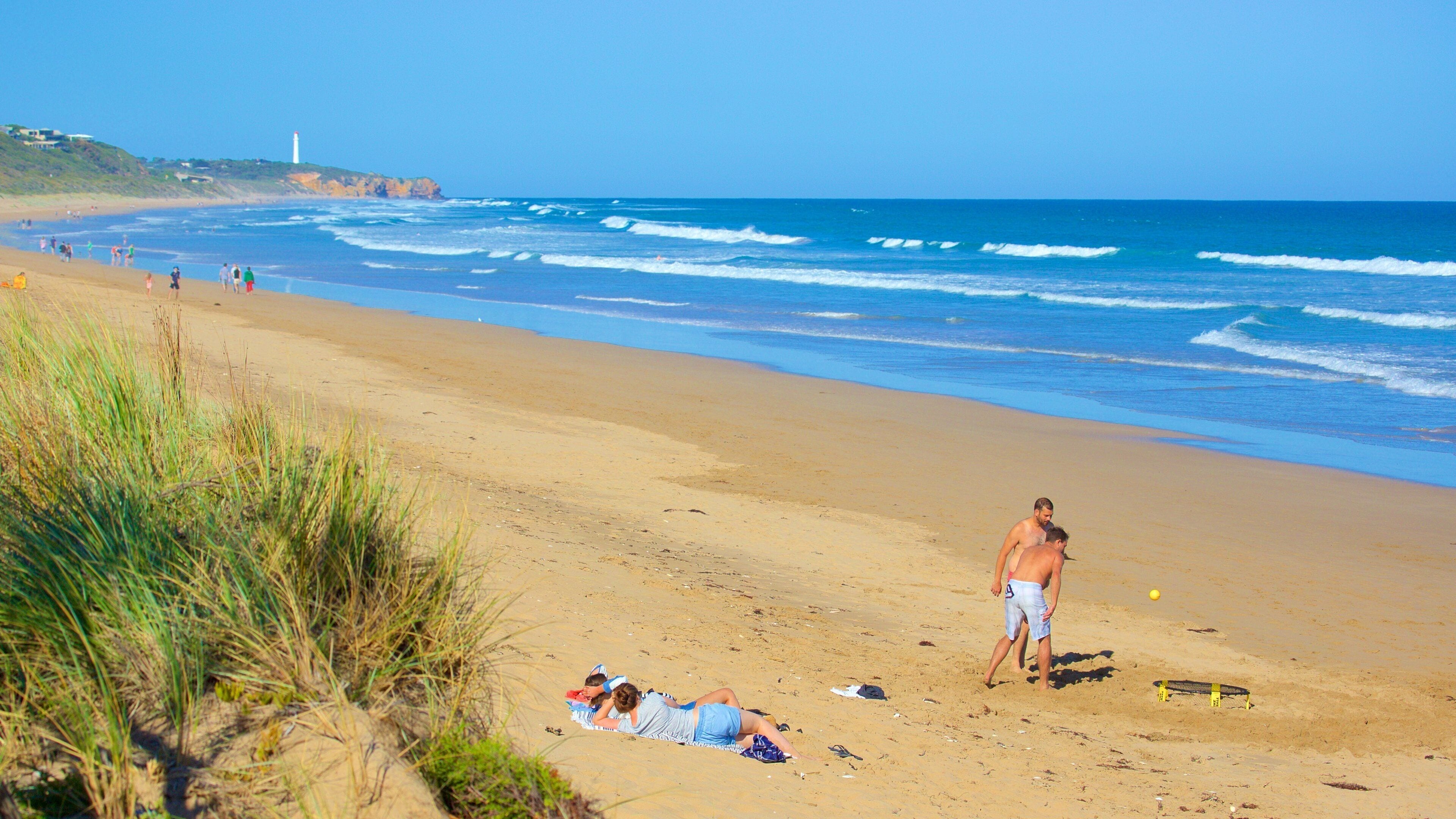 A beach with waves, a lighthouse, and people.