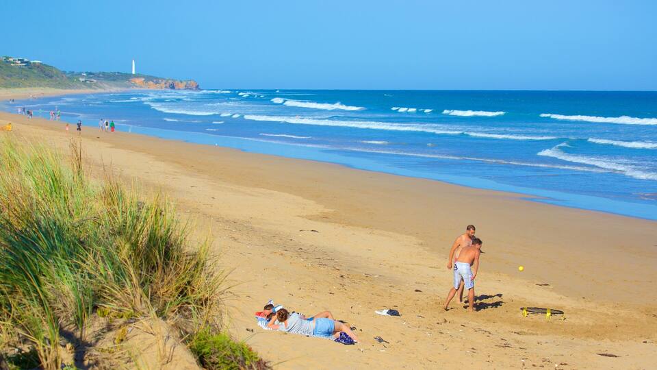 A beach with waves, a lighthouse, and people.