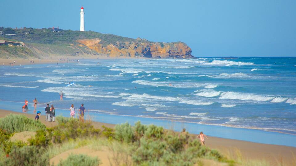 A beach with waves, a lighthouse, and people.