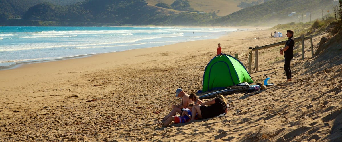 A sandy beach with a green tent, a wooden fence, and a hilly landscape in the background.