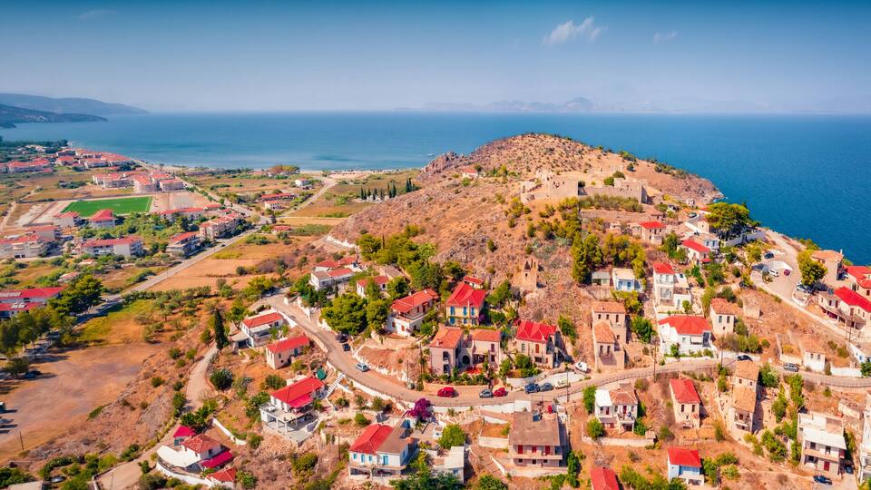 A coastal town with red-roofed houses, a hilltop fortress, and a view of the sea.