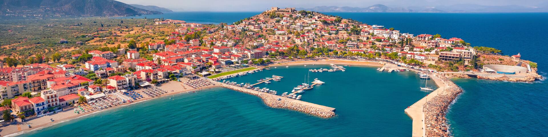 Panonoramic view from flying drone of Astros port. Sunny summer seascape of Myrtoan Sea. Aerial urban scene of Arcadia region, Greece, Europe. Traveling concept background.