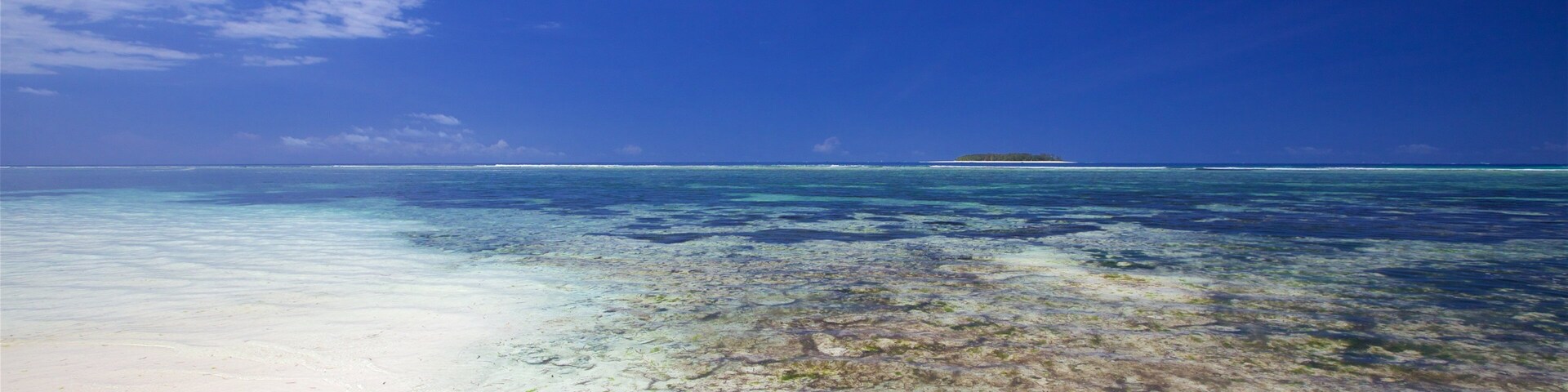 Mar turquesa transparente, arena blanca y una isla a lo lejos.