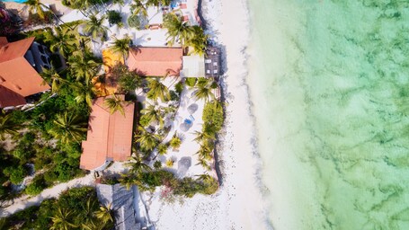 Ein Luftbild einer Küstenlandschaft mit Strand, Palmen und Gebäuden mit roten Dächern.