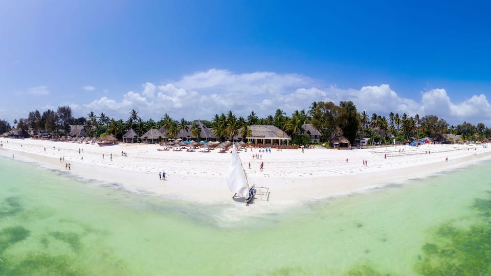A tropical island with a white sandy beach, clear turquoise waters, and a thatched-roof structure.