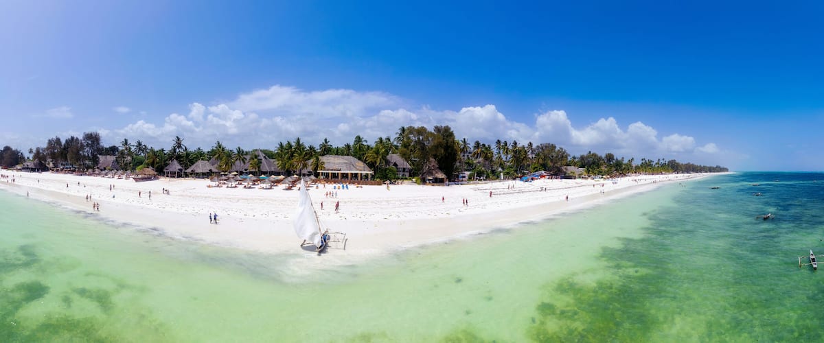 A tropical island with a white sandy beach, clear turquoise waters, and a thatched-roof structure.