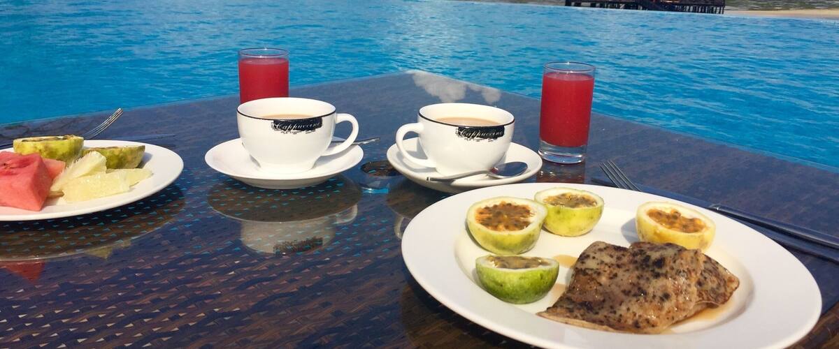 A table with breakfast by a pool overlooking the ocean.