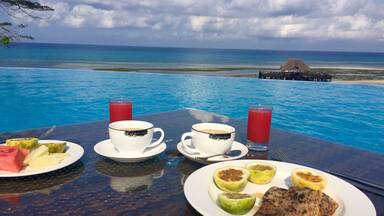 Mesa com café da manhã à beira de uma piscina com vista para o oceano.