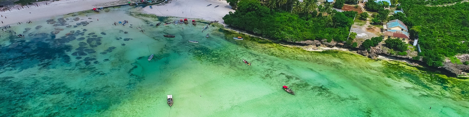 Vista aérea de una playa con aguas turquesas cristalinas, barcos y casas con techos coloridos.