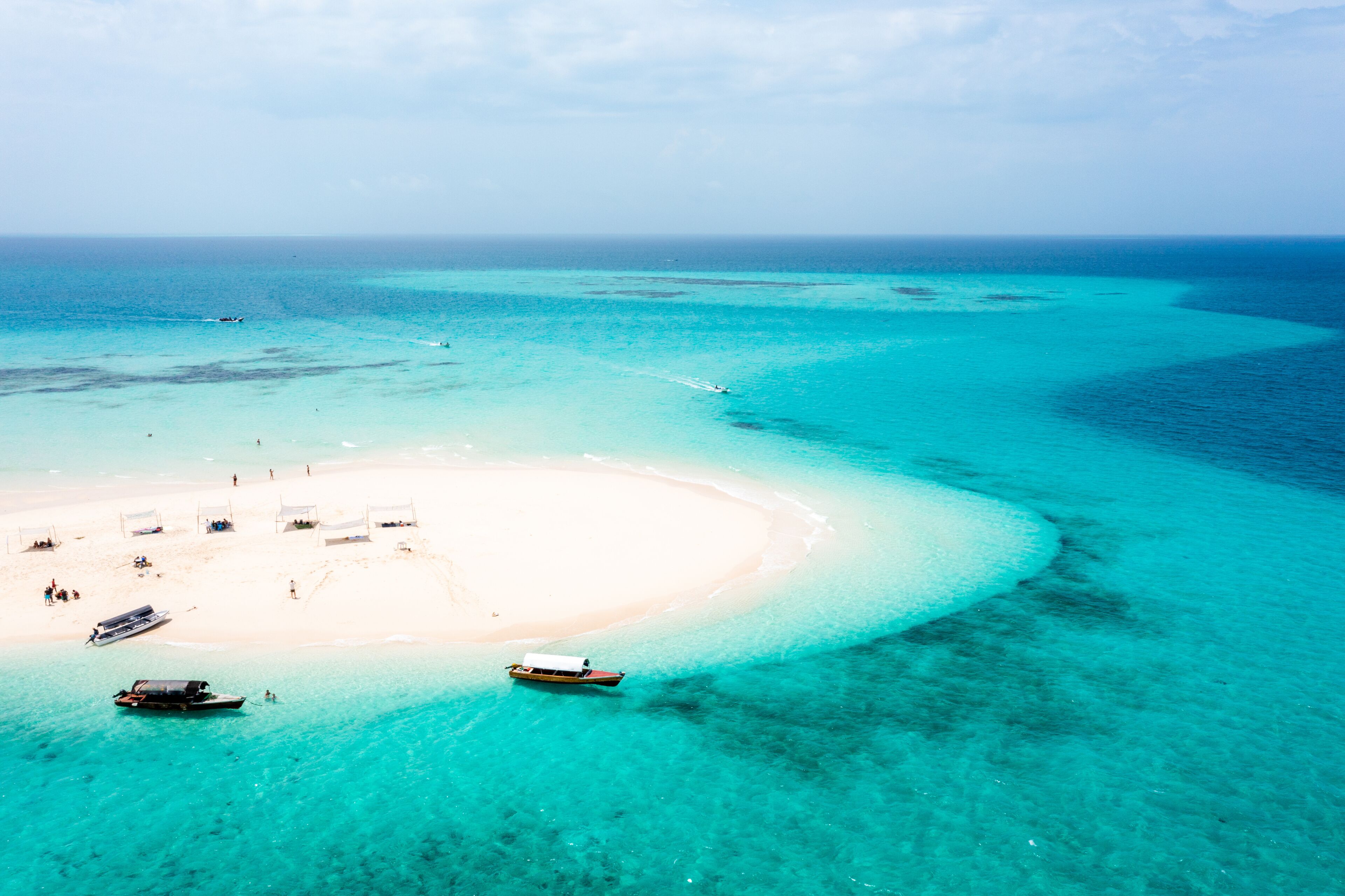 A turquoise lagoon with a white sandy beach, boats, and a clear blue sky.