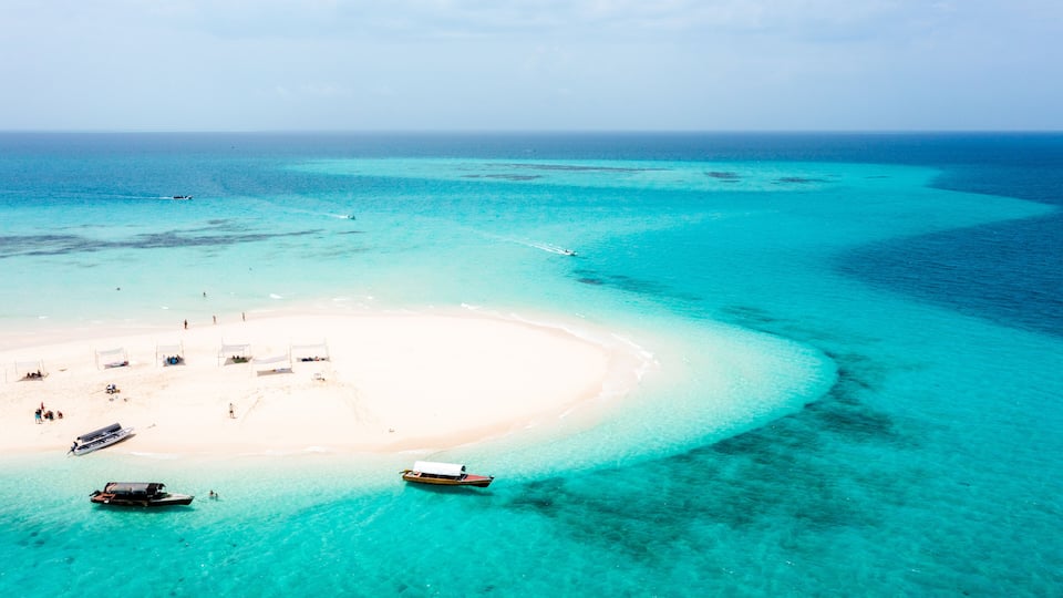 A turquoise lagoon with a white sandy beach, boats, and a clear blue sky.