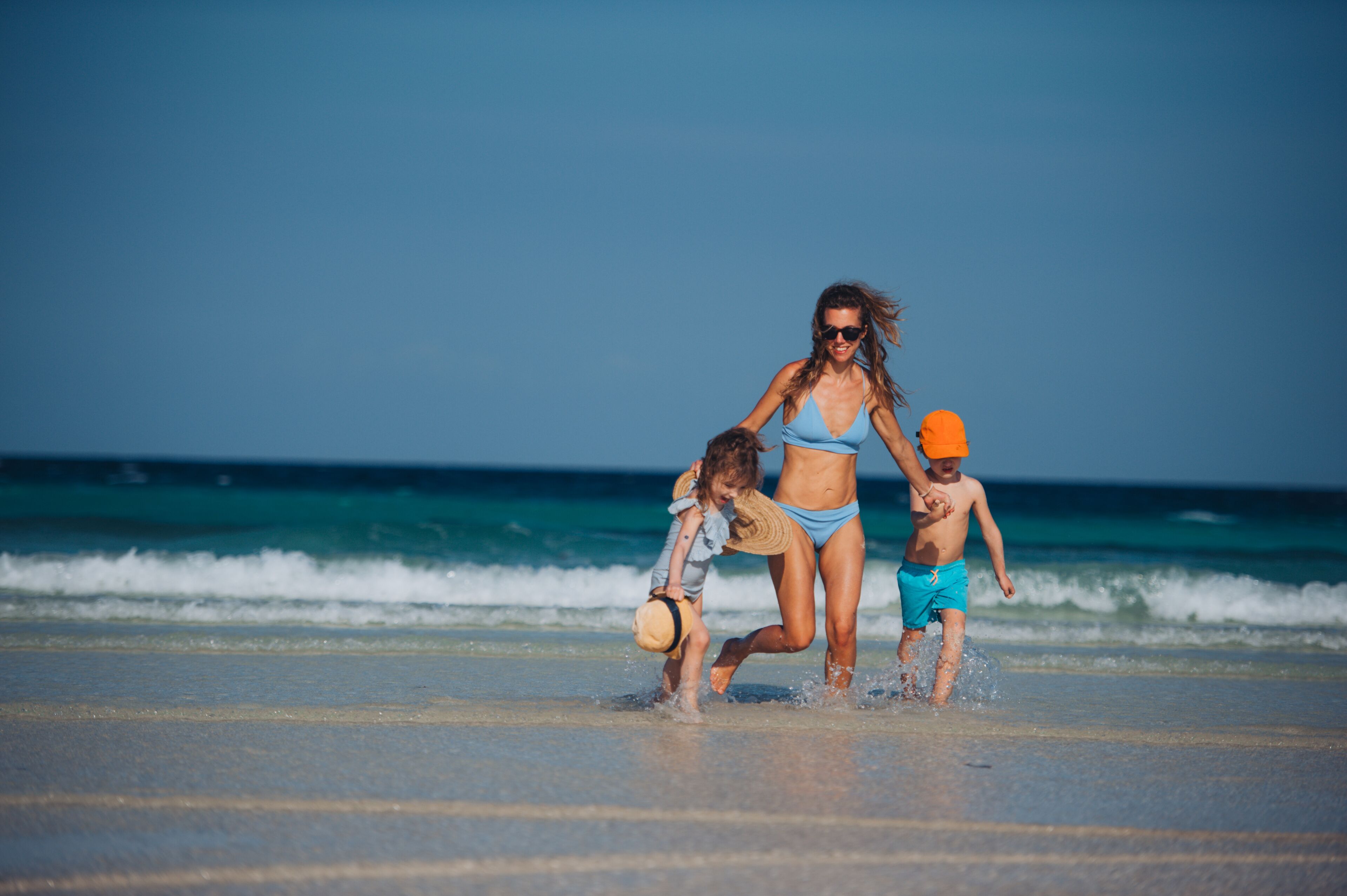 Young mother with little girl and boy walking on the beach.