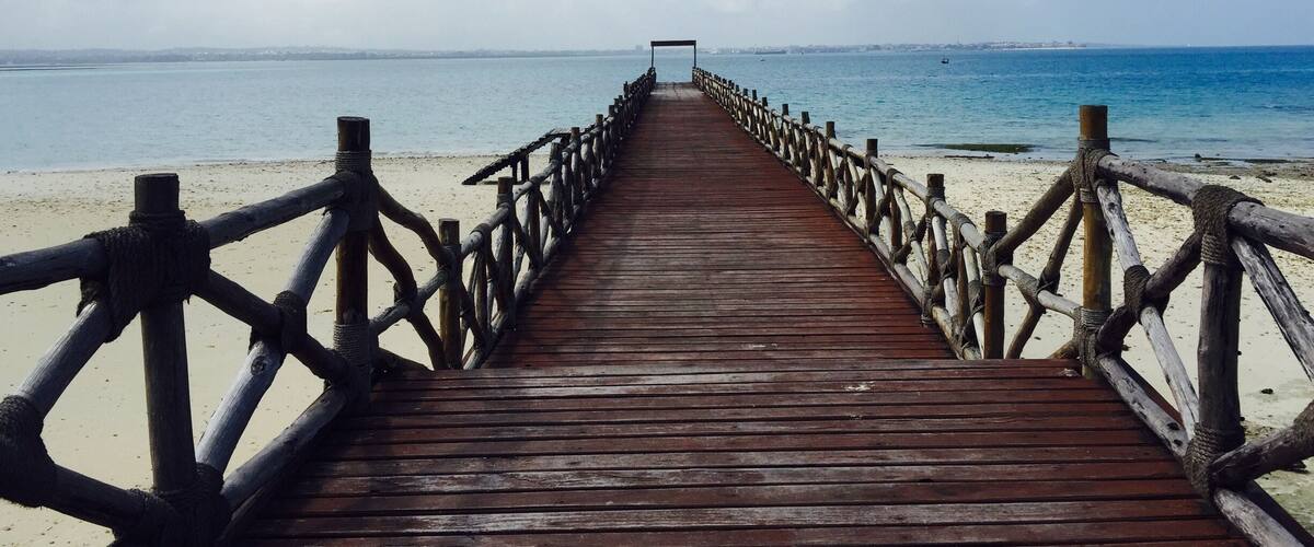 A wooden pier leading to a beach with a clear sky.
