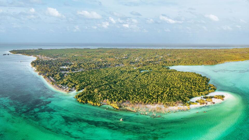 An aerial view of a tropical island with clear turquoise waters, dense green forest, and a small beach area.