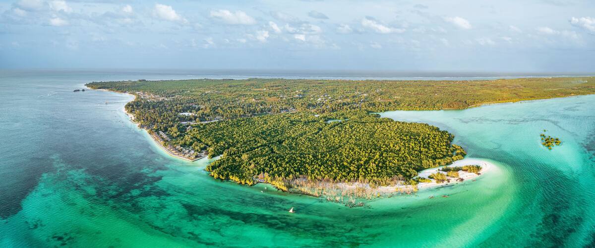 An aerial view of a tropical island with clear turquoise waters, dense green forest, and a small beach area.