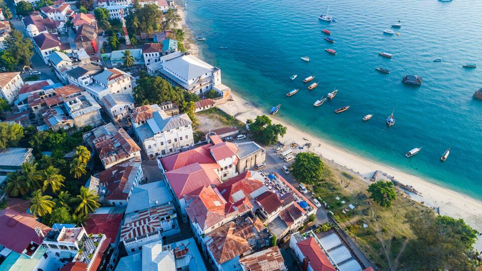 Vista aérea de uma cidade costeira com edifícios, praia e vários barcos.
