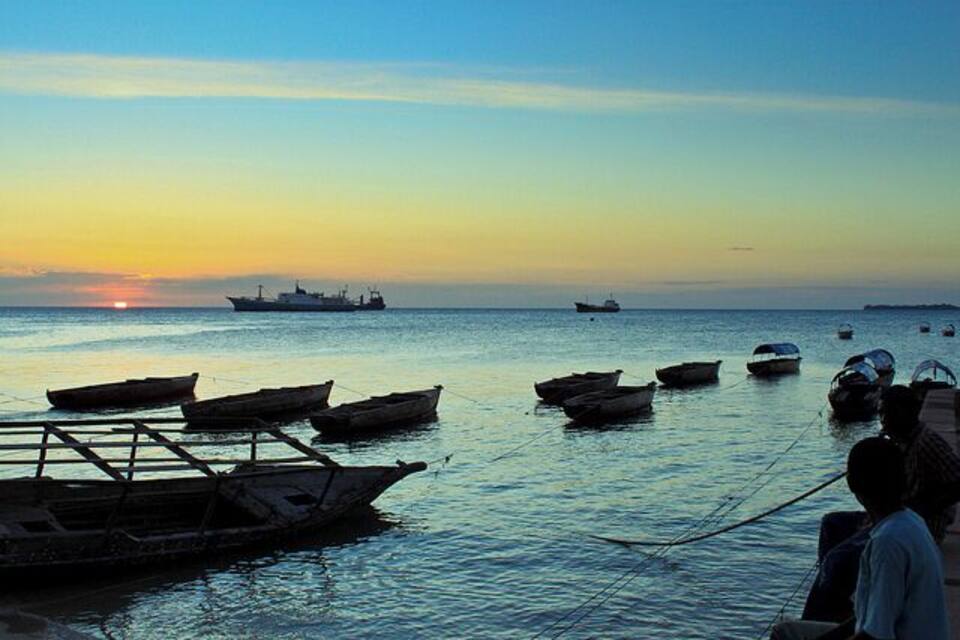 Une mer calme au coucher du soleil, avec plusieurs bateaux et un grand navire à l’horizon.