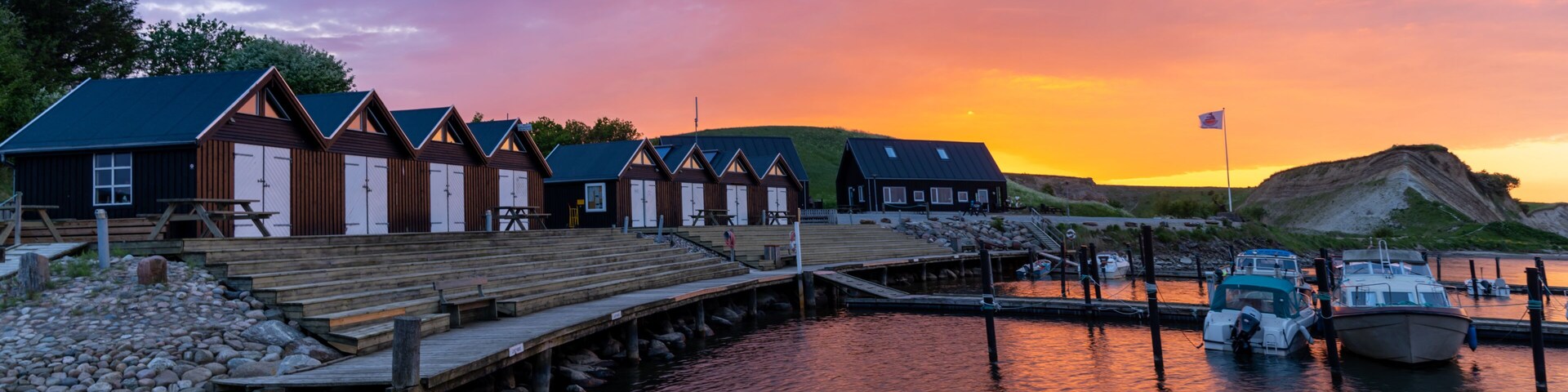 Um cais com edifícios de madeira, um píer e barcos ao pôr do sol.